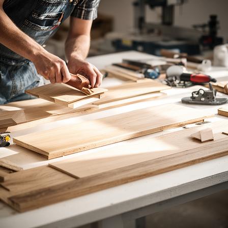 Schreinerin beim Möbelbau an einer hellen Werkbank mit Holzplatten und Werkzeugen